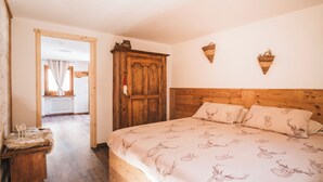 A bedroom with a wooden headboard, a bed with a deer print bedspread, a wooden nightstand, and a rustic wooden wardrobe.
