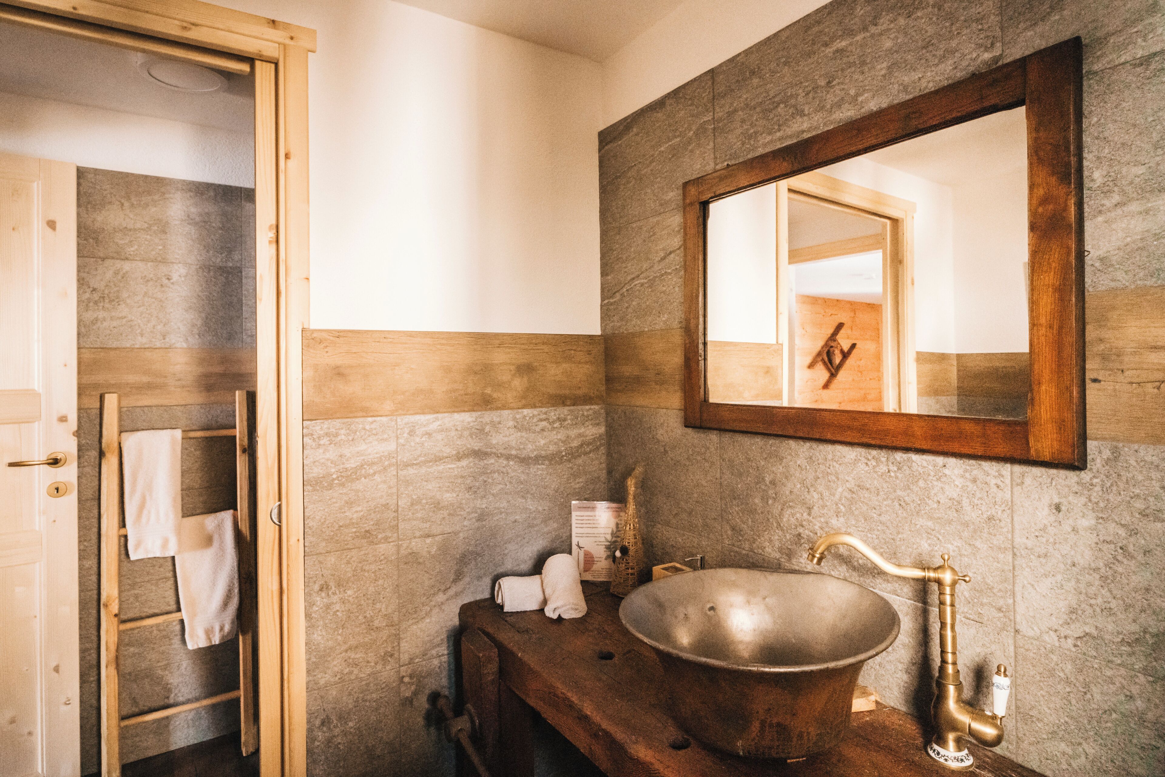 Ein Badezimmer mit einem hölzernen Waschtisch, einem großen Becken, einer Holzleiter und einem Spiegel an der Wand.
