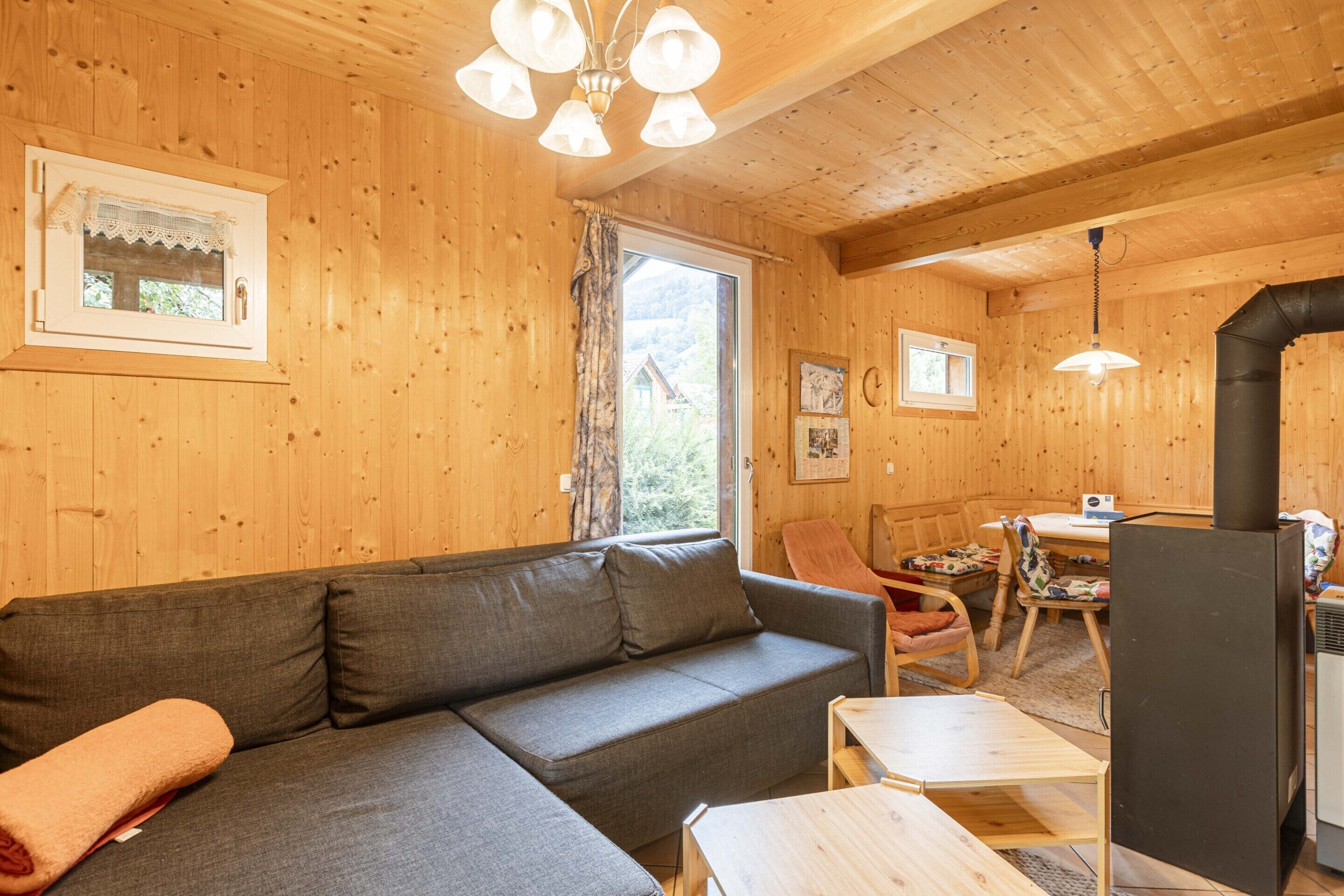 Interno di una baita in legno con divano, tavolo, sedia, camino e finestra con tende.