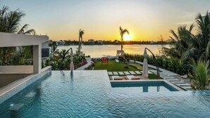Piscina com vista para o pôr do sol, rodeada por palmeiras e um gramado bem cuidado.
