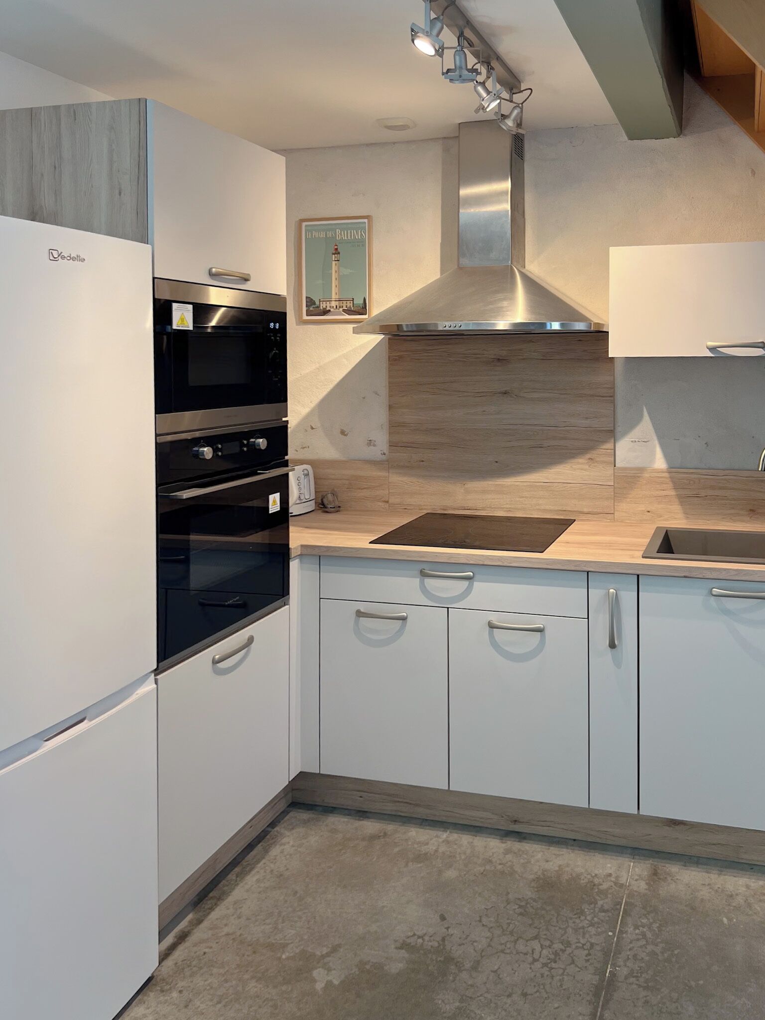 Una cocina moderna con armarios blancos, horno empotrado y campana extractora de acero inoxidable.