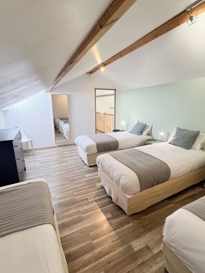 Un'ampia camera mansardata con soffitto alto, travi a vista in legno e un'ampia finestra a lucernario. Sono presenti due letti con biancheria coordinata e un piccolo angolo studio.