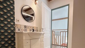 Casa de banho com uma pia branca, um espelho e parede com padrão.