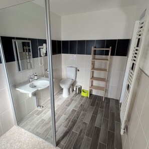 Un bagno con cabina doccia in vetro, lavandino, water e ripiano in legno.