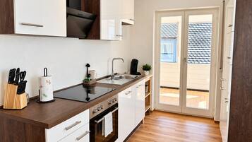 Una cocina moderna con una isla central, horno empotrado y puerta corredera de cristal que da a un espacio exterior.