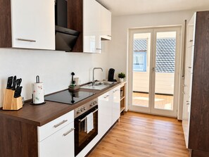 Una cocina moderna con una isla central, horno empotrado y puerta corredera de cristal que da a un espacio exterior.