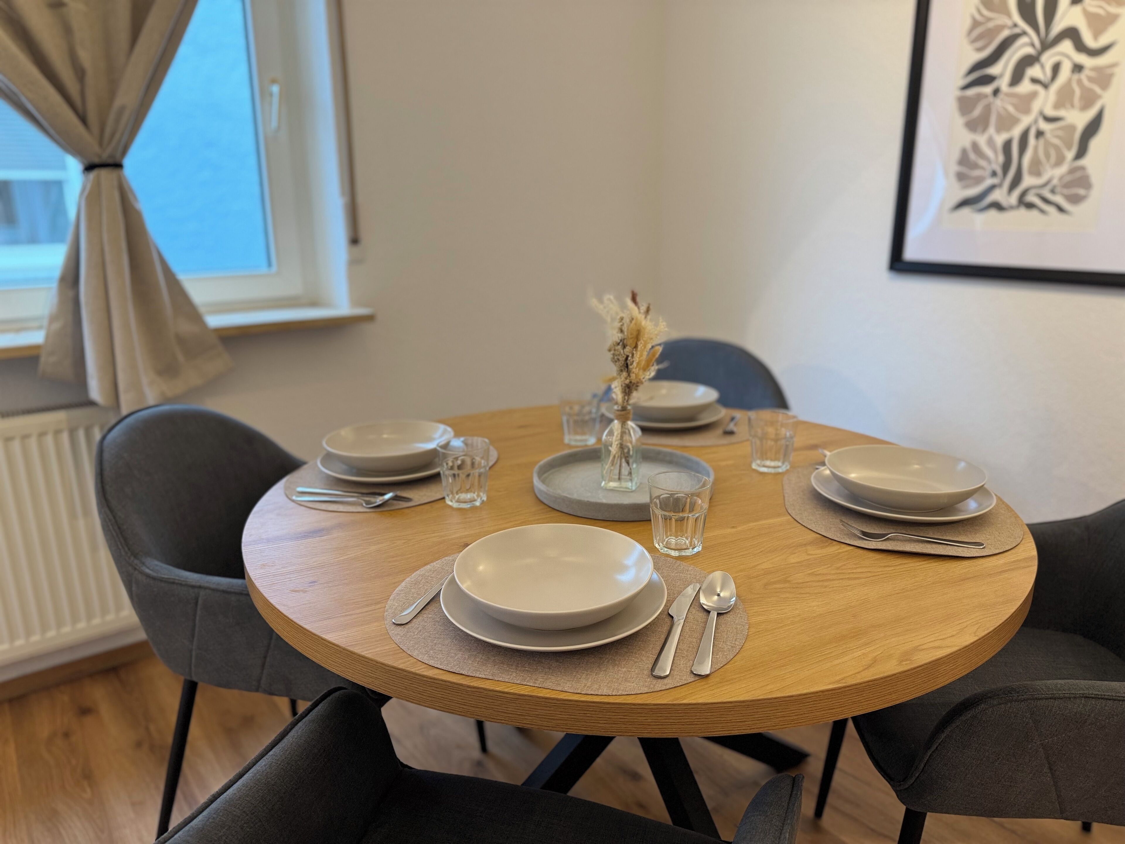 Una mesa de comedor dispuesta con platos, vasos y cubiertos, rodeada de sillas.