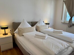 Une chambre d’hôtel avec deux lits, une table de chevet avec une lampe, une fenêtre avec des rideaux et un radiateur.