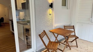 Une table et des chaises en bois sur un balcon, avec un mur blanc à la texture particulière et une fenêtre.