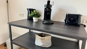 Una mesa de madera oscura con una cafetera negra, una pequeña planta en maceta y un altavoz negro.