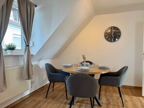 A dining area with a round table, four chairs, a clock on the wall, and a window with curtains. - Apartment StadtUfer - Top location & close to the lake (Friedrichshafen)