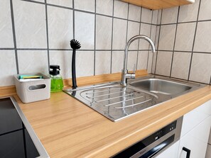 A kitchen with a stainless steel sink, a dish rack, a soap dispenser, and a storage bin. - StadtUfer Apartment - Prime Location & Close to the Lake (Friedrichshafen)