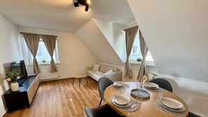 Un comedor con una mesa de madera dispuesta para cuatro personas, un sofá y un televisor sobre un mueble.