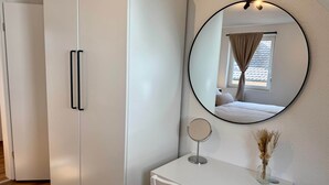 Un dormitorio con un armario blanco, una mesita de noche con espejo y una ventana con cortinas.