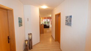 Ein Flur mit Holztüren, Holzdielen und Blick in einen Wohnbereich mit einer Couch und Vorhängen.