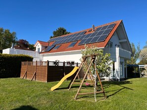 A house with a solar panel roof, a wooden swing set, and a fenced yard. - Vacation apartment ground floor (Altenkirchen)