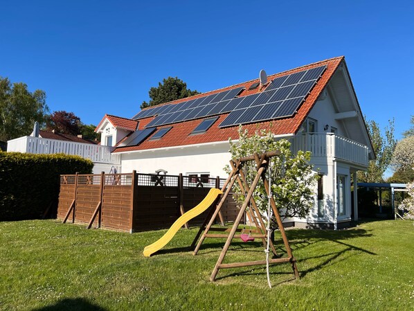 A house with a solar panel roof, a wooden swing set, and a fenced yard. - Ground-floor vacation apartment (Altenkirchen)