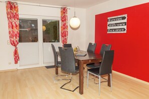 A dining area with a wooden table, black chairs, and a red accent wall. - Ground-floor vacation apartment (Altenkirchen)
