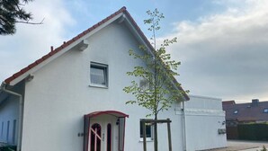 Ein weißes Haus mit roter Tür und einem kleinen Baum im Vorgarten.