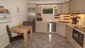 Eine kompakte Küche mit Kühlschrank, Geschirrspüler und Backofen. Ein Esstisch mit Stühlen steht dort, über dem Spülbecken befindet sich ein Fenster.