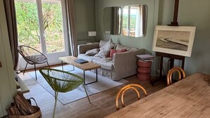 Ett modernt vardagsrum med en matplats, stora fönster och en hängande lampa.