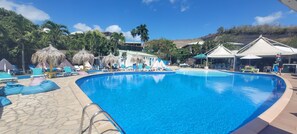 Une piscine entourée de chaises longues et de parasols, bordée de palmiers et avec une chaîne de montagnes en toile de fond.