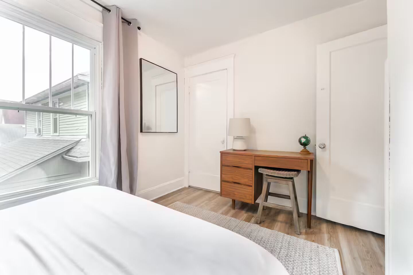 A bedroom with a bed, a wooden desk, a chair, a lamp, a globe, and a window with curtains.
