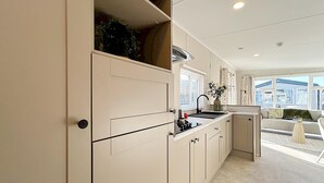 Cocina compacta con lavaplatos, estufa y armarios, que da paso a un comedor con sofá y vistas al exterior.