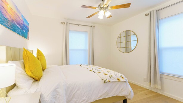 Ein Schlafzimmer mit Bett, Deckenventilator, Nachttisch, Lampe und einem Bild an der Wand.