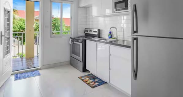 Une cuisine moderne avec des armoires blanches, des appareils en acier inoxydable et une vue sur l’extérieur.