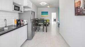 Eine moderne Küche mit weißen Schränken, einem Edelstahlkühlschrank und einer Mikrowelle. Im Hintergrund ist ein Essbereich mit Tisch und Stühlen zu sehen.