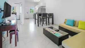 Ein modernes Wohnzimmer mit einer Couch, einem Couchtisch und einem Fernseher. Es gibt einen Essbereich mit Stühlen und einem Tisch.