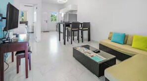 A modern living room with a sofa, a coffee table, and a TV. There is a dining area with chairs and a table. - Spacious 2 Bedroom Condo with AC in Turks and Caicos Near Beach (Venetian Road Settlement)