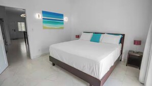 Ein Schlafzimmer mit einem großen Bett, weißen Wänden, einem Bild und einem Nachttisch mit einer Lampe.