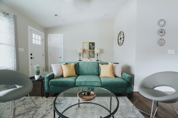 Un salon avec un canapé vert, deux fauteuils, une table basse et une petite table d’appoint sur laquelle est posée une plante.
