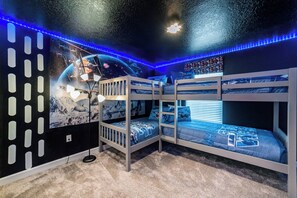 Une chambre avec des lits superposés, décorée d’une fresque sur le thème de l’espace, éclairée par des lumières LED bleues et dotée d’un luminaire au plafond.