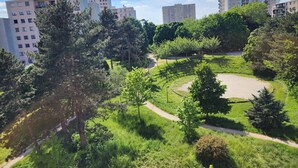 A park with a circular walking path, surrounded by trees and greenery, with residential buildings in the background. - 3-bedroom apartment between Paris and Disneyland - 82m3 - Close to transport links (Neuilly-sur-Marne)