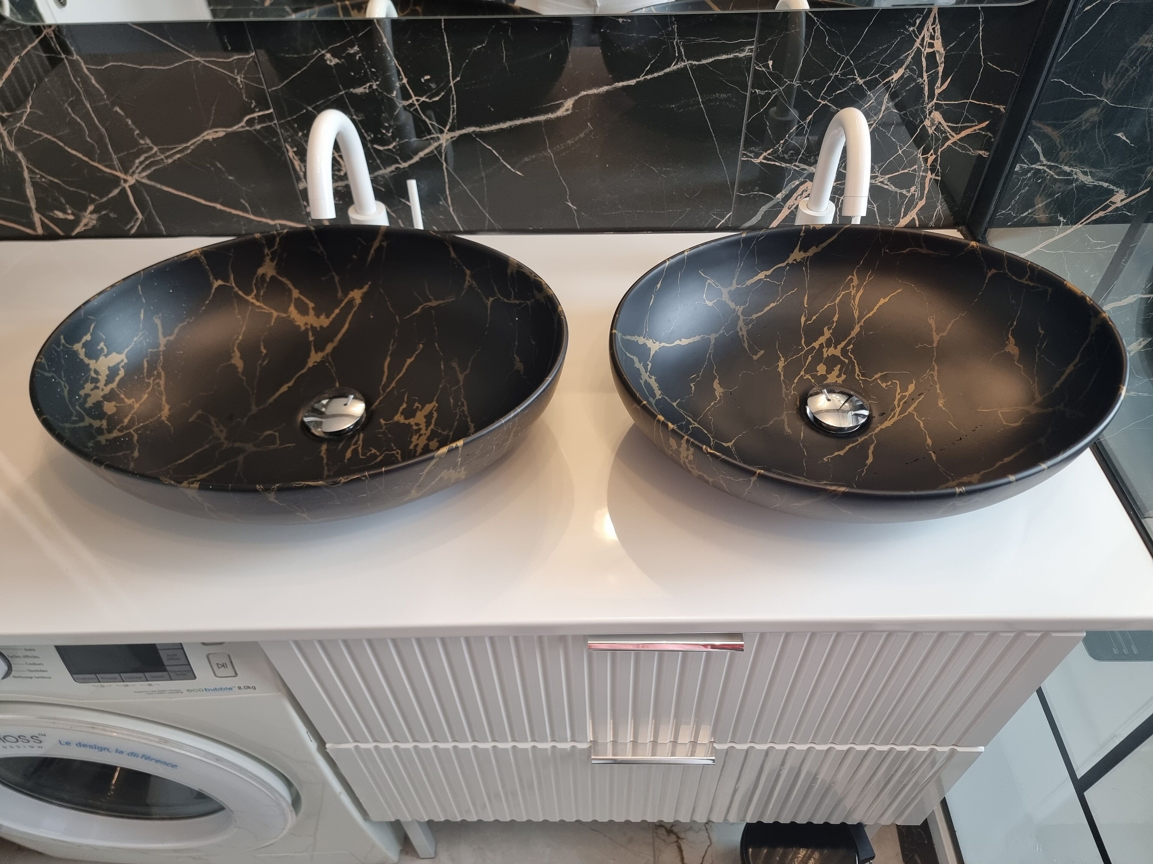 Un baño con dos lavamanos de mármol negro, una encimera blanca y una lavadora.