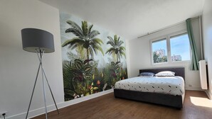 A bedroom with a large mural of tropical plants, a modern bed, and a floor lamp. - 3-bedroom apartment between Paris and Disneyland - 82m3 - Close to transport links (Neuilly-sur-Marne)
