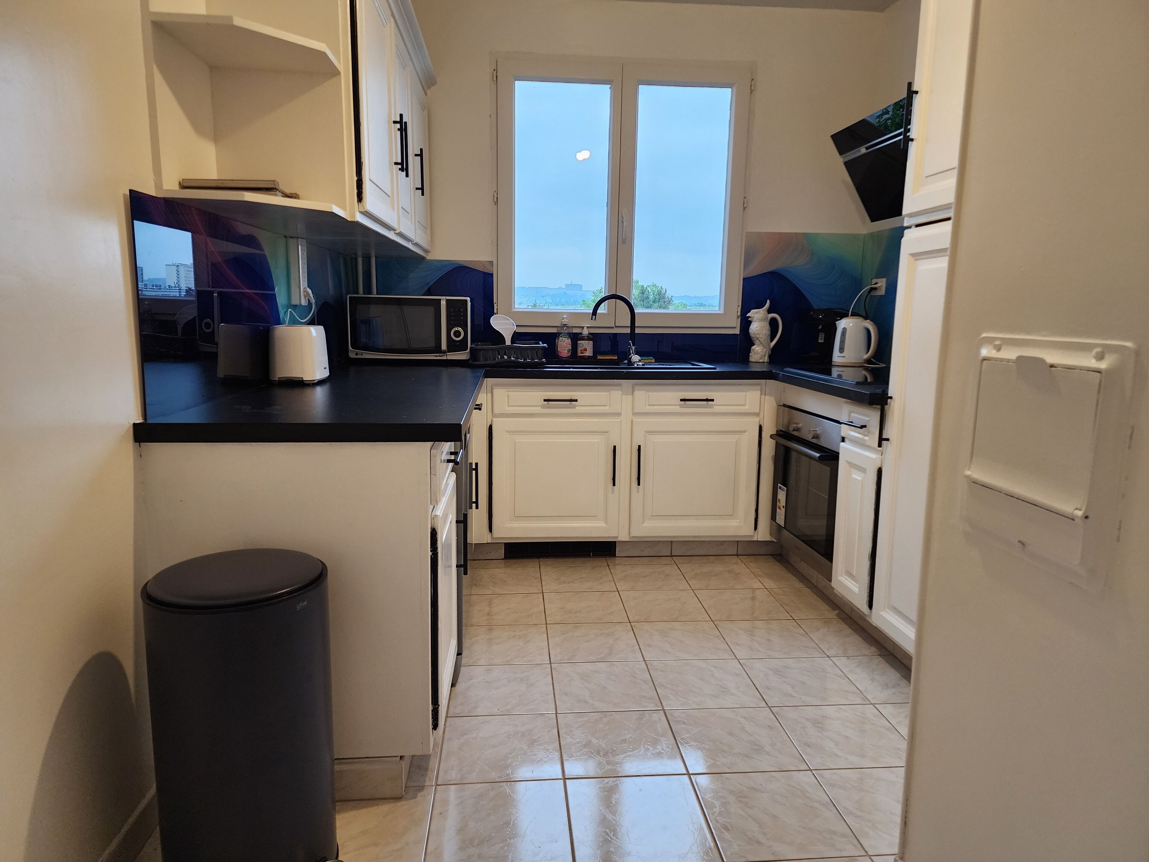Cocina compacta con armarios blancos, microondas, fregadero y ventana con vistas.