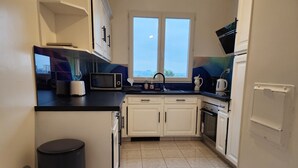 A compact kitchen with white cabinets, a microwave, a sink, and a window with a view. - 3-bedroom apartment between Paris and Disneyland - 82m3 - Close to transport links (Neuilly-sur-Marne)