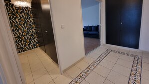 A hallway with a patterned wall, a patterned rug, a dark door, and a light fixture. - 3-bedroom apartment between Paris and Disneyland - 82m3 - Close to transport links (Neuilly-sur-Marne)