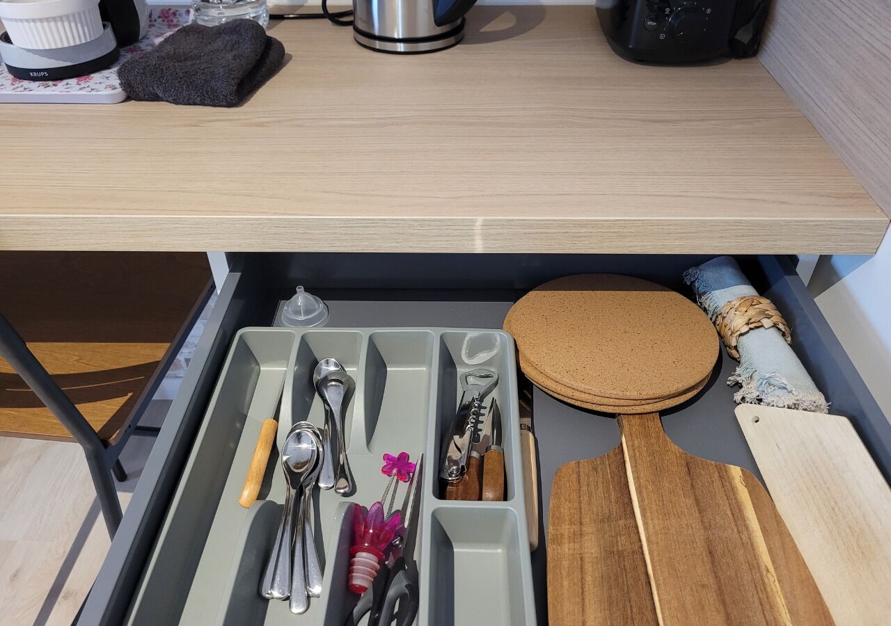 Un cajón con utensilios de cocina, una paleta de corcho y una tabla de cortar de madera.