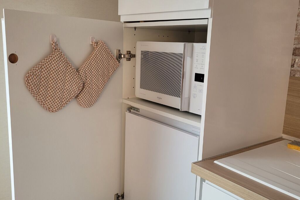 Een keuken met een magnetron en oven, een geruit ovenwanten hangt aan de muur, en een houten aanrecht.