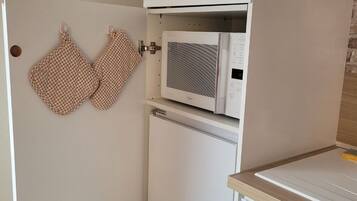 Een keuken met een magnetron en oven, een geruit ovenwanten hangt aan de muur, en een houten aanrecht.