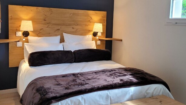 Uma cama com cabeceira de madeira, duas luminárias de apoio e um cobertor escuro.