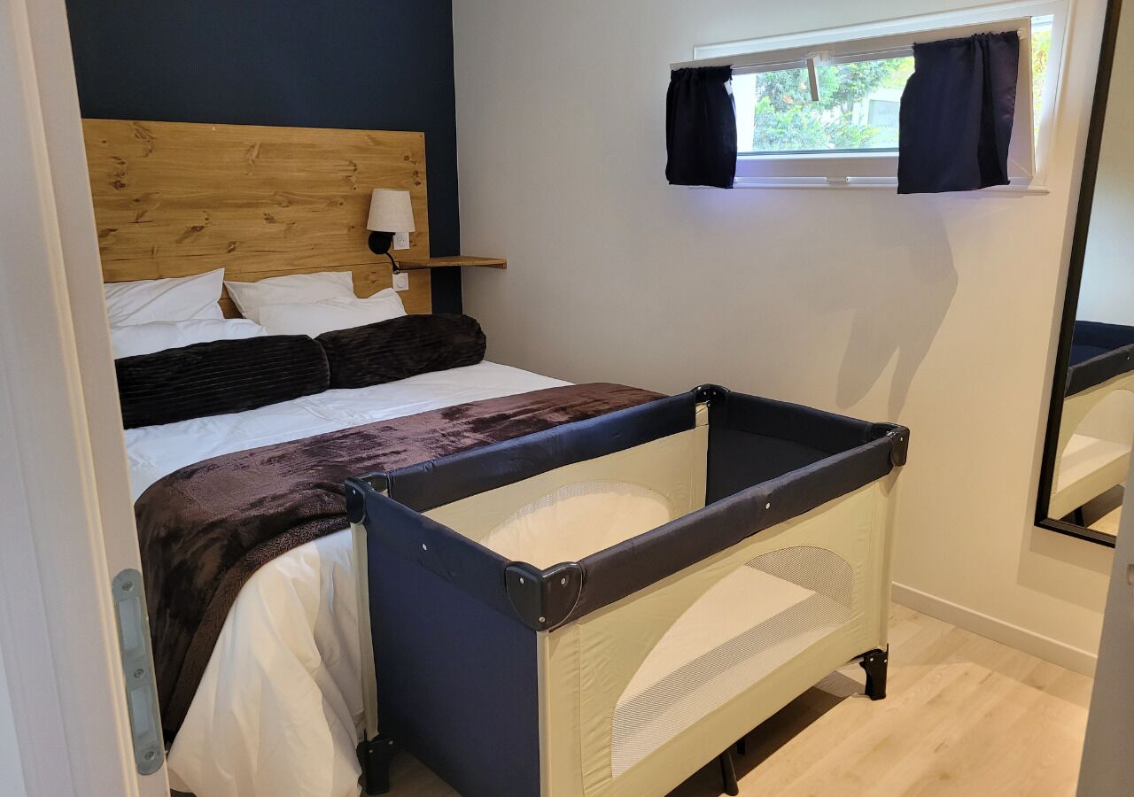 Een slaapkamer met een bed, een ledikant, een raam met gordijnen en een spiegel.