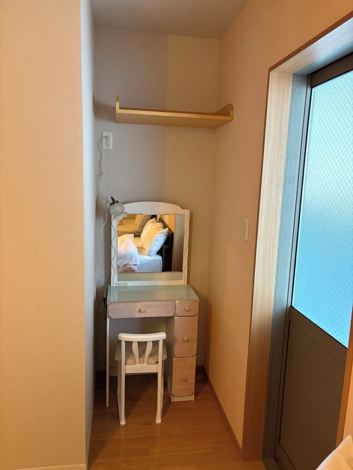 A small bedroom with a bed, a desk, and a chair. There is a window with a view of the outside.