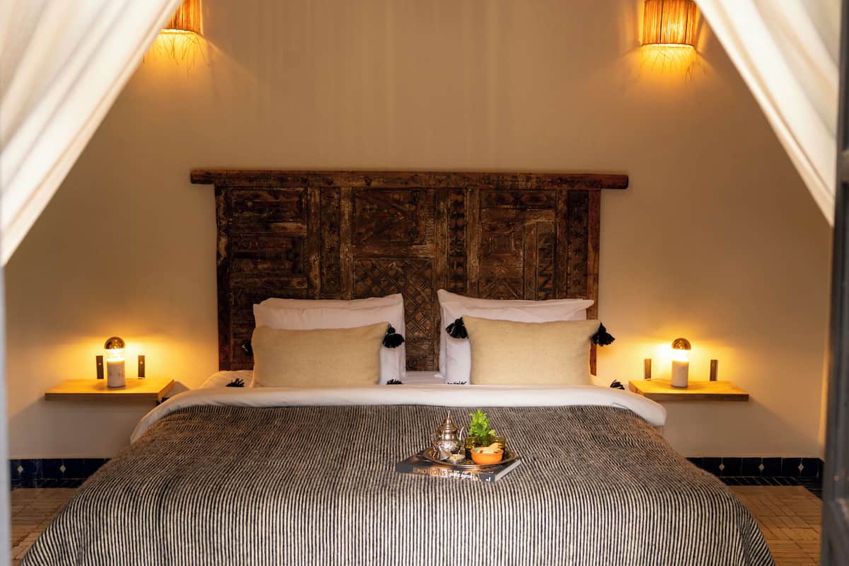 A bed with a wooden headboard, two bedside tables with lamps, and a tray with decorative items on the bed.