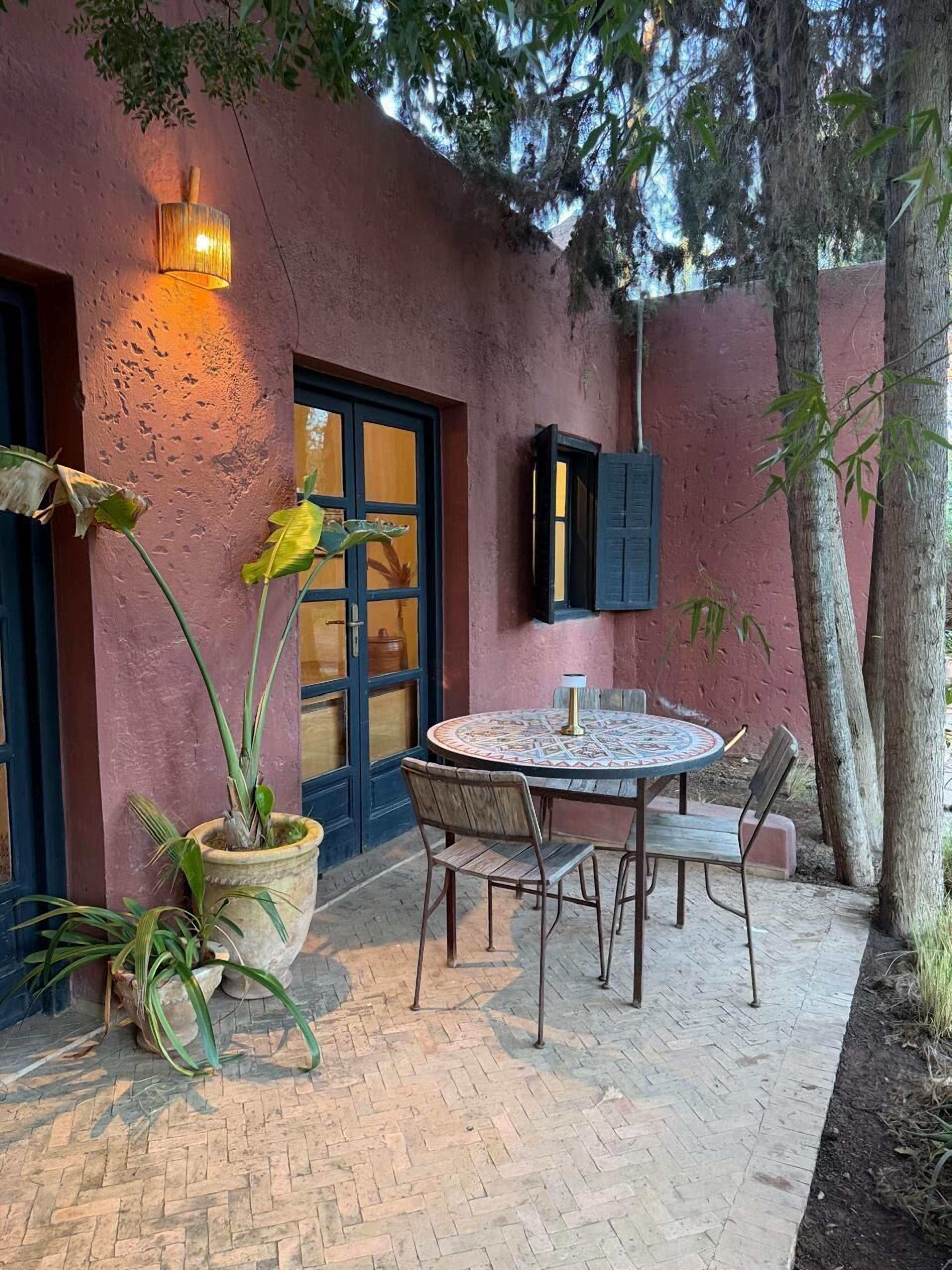 Un patio con un tavolo rotondo e sedie, una pianta in vaso, una lampada a parete e una porta con un oblò.